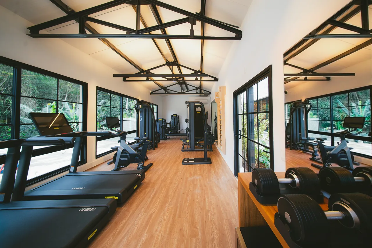Sala de musculação com piso de madeira e janelas altas